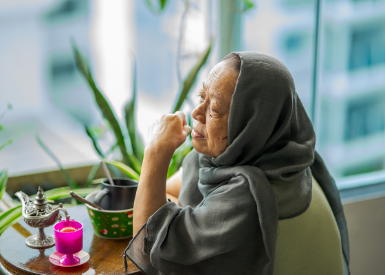 Image of woman with head scarf sitting next to window with teapot