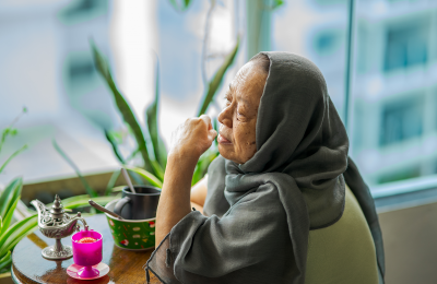 Image of woman with head scarf sitting next to window with teapot